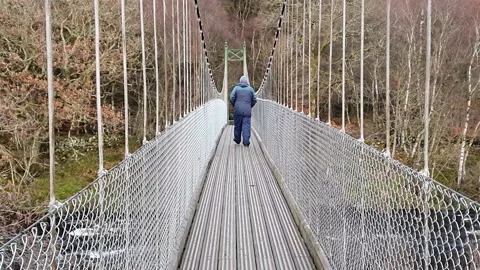 Man walking and looking over a suspension bridge at the river below, Scotland Stock Footage 147600912