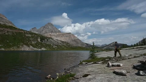 Man walking away from the camera along the rocky shoreline of a mountain lake.   Stock Footage 256592157