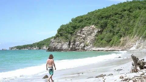 Man walking away from camera next the ocean while waves crash on the beach Stock Footage 219661150