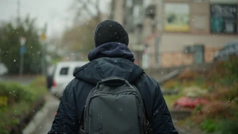 Man Walking Away in Light Snow with Backpack on Urban Street with winter cold Stock Footage 346658614