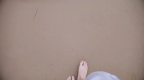 Man walking bare foot on sandy beach into ocean wave, point of view Stock Footage 64961057