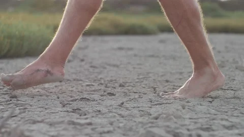 Man walking barefoot on bottom of dried lake or cracked soil ground. Side view Stock Footage 196822476