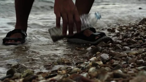 A man walking on the beach bends down to pick up a plastic bottle Stock Footage 317883072