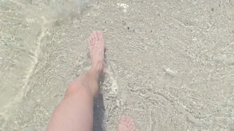Man walking at a beach in a day, waves edge foaming gently beneath them Stock Footage 134631771