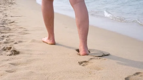 Man walking on the beach next to the sea leaving footprints on sand view from Stock Footage 311144948