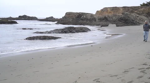 Man walking  on beach by ocean on overcast day Видео 67877551