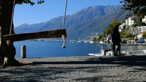 Man Walking Behind an Empty Swing over Alpine Lake Maggiore Stock Footage 191952568