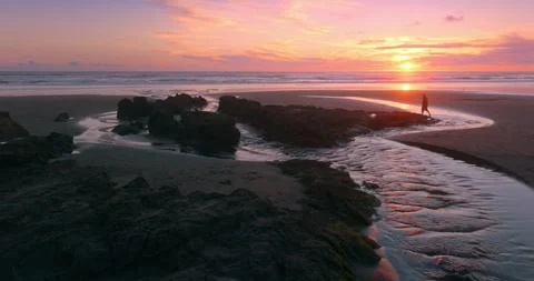 Man walking in a calm stream flowing into the ocean at sunset giving the feeling Stock Footage 279614694