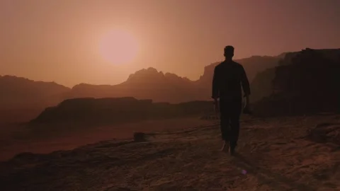 Man walking with a camera towards a red sunset in Wadi Rum, Jordan desert Stock Footage 308327603