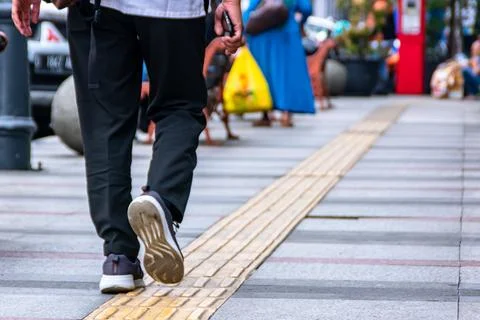 Man walking on the city pavement while holding his phone Stock Photos