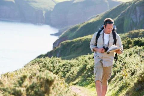 Man walking on cliffside path looking at map Stock Photos