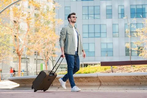 Man walking confidently with a suitcase while enjoying a sunny day in a vibrant Stock-Fotos