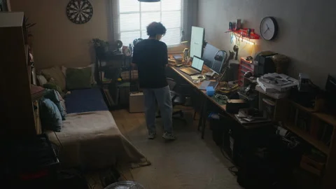 Man Walking to Desk and Starting to Work on Laptop in Messy Room Stock Footage 338424908