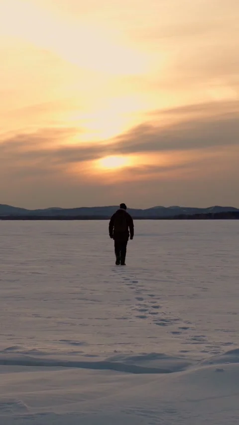 A man walking into the distance at sunset on the snow cover of a frozen lake. Stock Footage 313858074