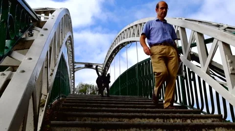 Man walking with dog down steps if a arched bridge Stock Footage 44541019