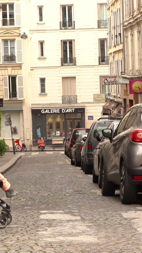 Man Walking Down Cobblestone Street With Parked Cars in Urban Art District Stock Footage 334954333