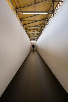 Man walking down a corridor towards a well lit end exit Stock Photos