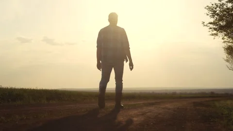 Man walking down dirt road. Silhouette of farmer walking in a field. Farmer Stock Footage 320473814