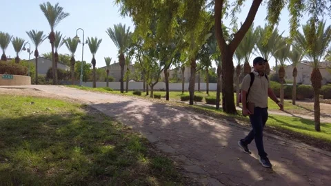 A man is walking down a path in a park. He is wearing a backpack and a hat. Stock Footage 324924268