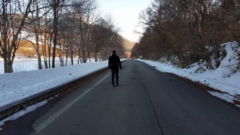 A man walking down a road lined by trees and snow in the Winter Stock Footage 104700610