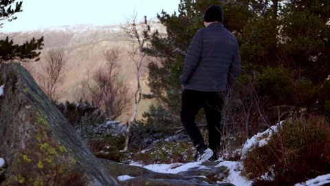 Man walking down snowy mountain with a stone in foreground Stock Footage 233513984