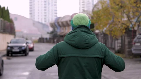 Man walking down the street putting headphones on his head view from behind Stock Footage 313392609