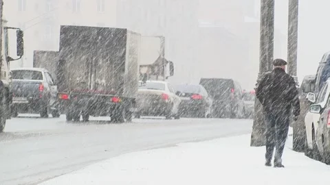 Man is walking down the street in the snow storm. Traffic jam on the road. Stock Footage 148904174