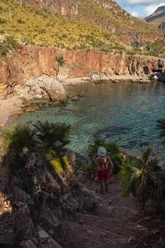 Man walking down trail to hidden rocky beach with clear turquoise sea Stock Photos