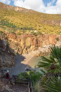 Man walking down trail to hidden rocky beach with clear turquoise sea Stock Photos