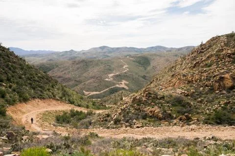 A man walking down on a winding dirt road in the desert Stock Photos