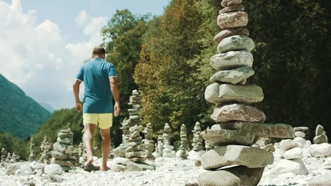 Man Walking In The Dry Riverbed In The Middle Of Stacked Stone Sculptures  Stock Footage 94032232