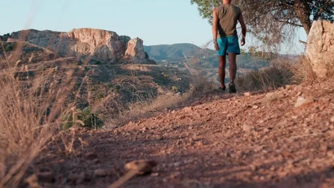 Man walking on dusty mountain path at golden hour, exploring arid landscape.. Stock Footage 340995810