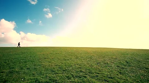 Man walking on the edge of a green hill with beautiful clouds above Stock Footage 48802084