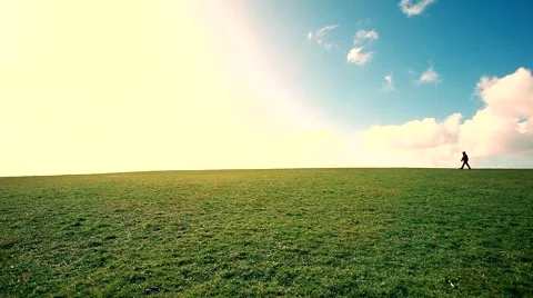 Man walking on the edge of a green hill with beautiful clouds above Stock Footage 48802403