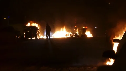 Man walking in foreground of fires burning in street at night with snow Stock Footage 78553977