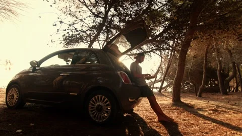 Man Walking Into Frame and Sitting to Work on Laptop at Car Trunk Stock Footage 341939040