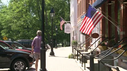 Man walking in front of stores with American Flags Stock Footage 8981516