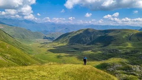 A man walking on a hiking trail with a view on green hills near the Chaukhi.. Stock Photos