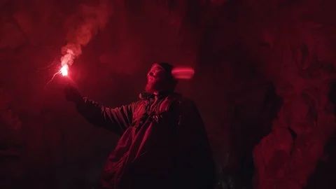 Man walking inside the mystical underground cave with a red burning signal flare Stock Footage 119225943