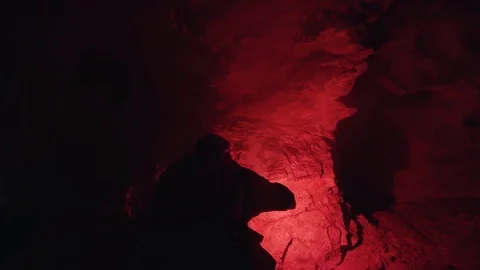 Man walking inside the mystical underground cave with a red burning signal flare Stock Footage 119225965