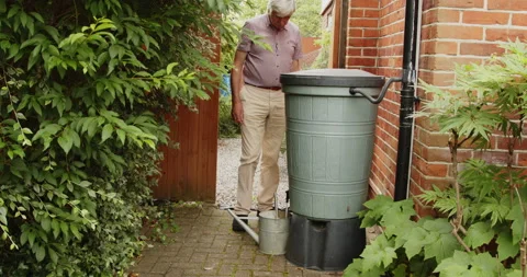 A man walking to a large grey water barrel filling a watering can 库存影片 158396914