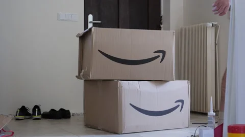 Man walking in large hall next to two large cardboard parcel boxes with Amazon Stock Footage 154970113