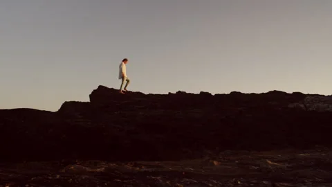 Man walking on a large rocky area at sunset by the ocean Stock Footage 279793362