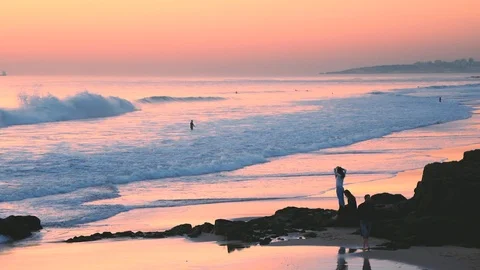 Man walking in low tide, sunset sky reflections on water at Carcavelos beach 動画素材 108916875