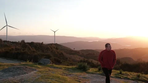 Man walking in mountains with wind turbines at sunset Stock Footage 344531182