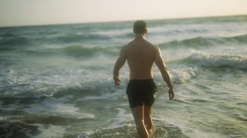 A man is walking in the ocean wearing only a black swim trunks Stock Footage 297949463
