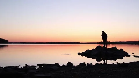 Man walking out onto rocks upon a lake at sunset in the late summer dusk. Stock Footage 233209777