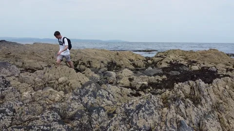 Man walking over rocks by sea Stock Footage 137910486