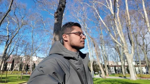 Man walking in a park during a clear day with trees in the background Stock Footage 346017417
