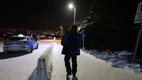 Man walking past car park in Tromso, Norway whilst it's snowing at night Stock Footage 301551888